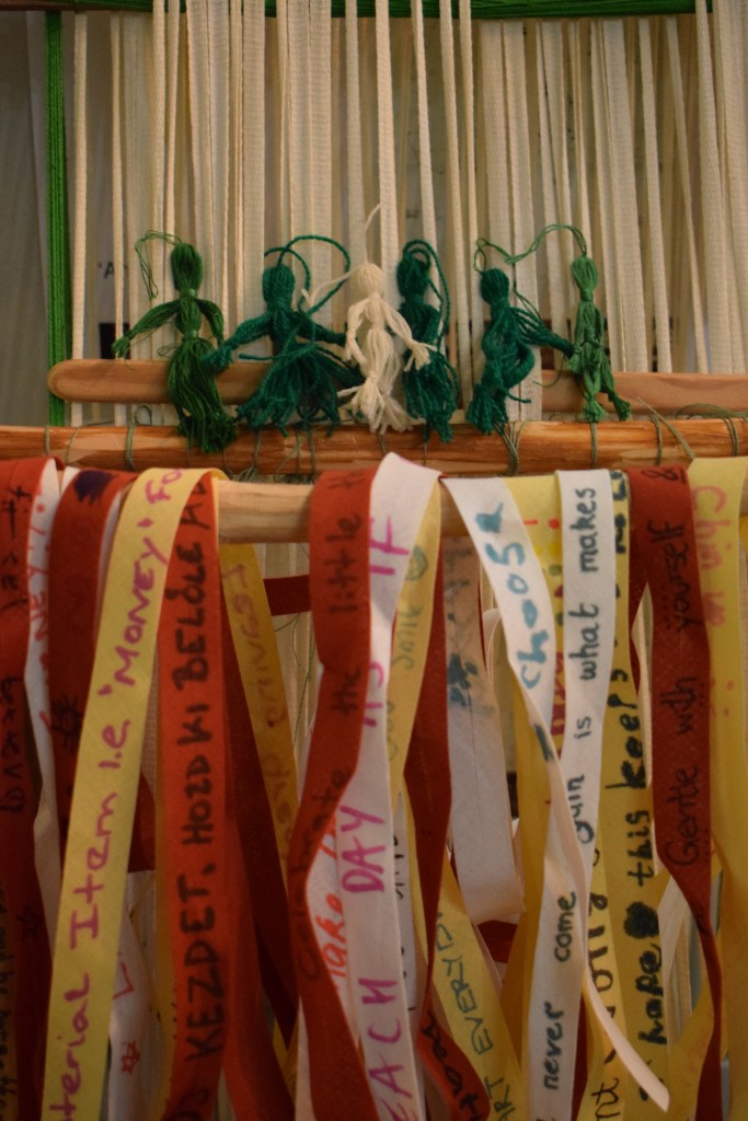 Lots of cloth tapes with handwritten notes on hang waiting to be woven onto the loom.
