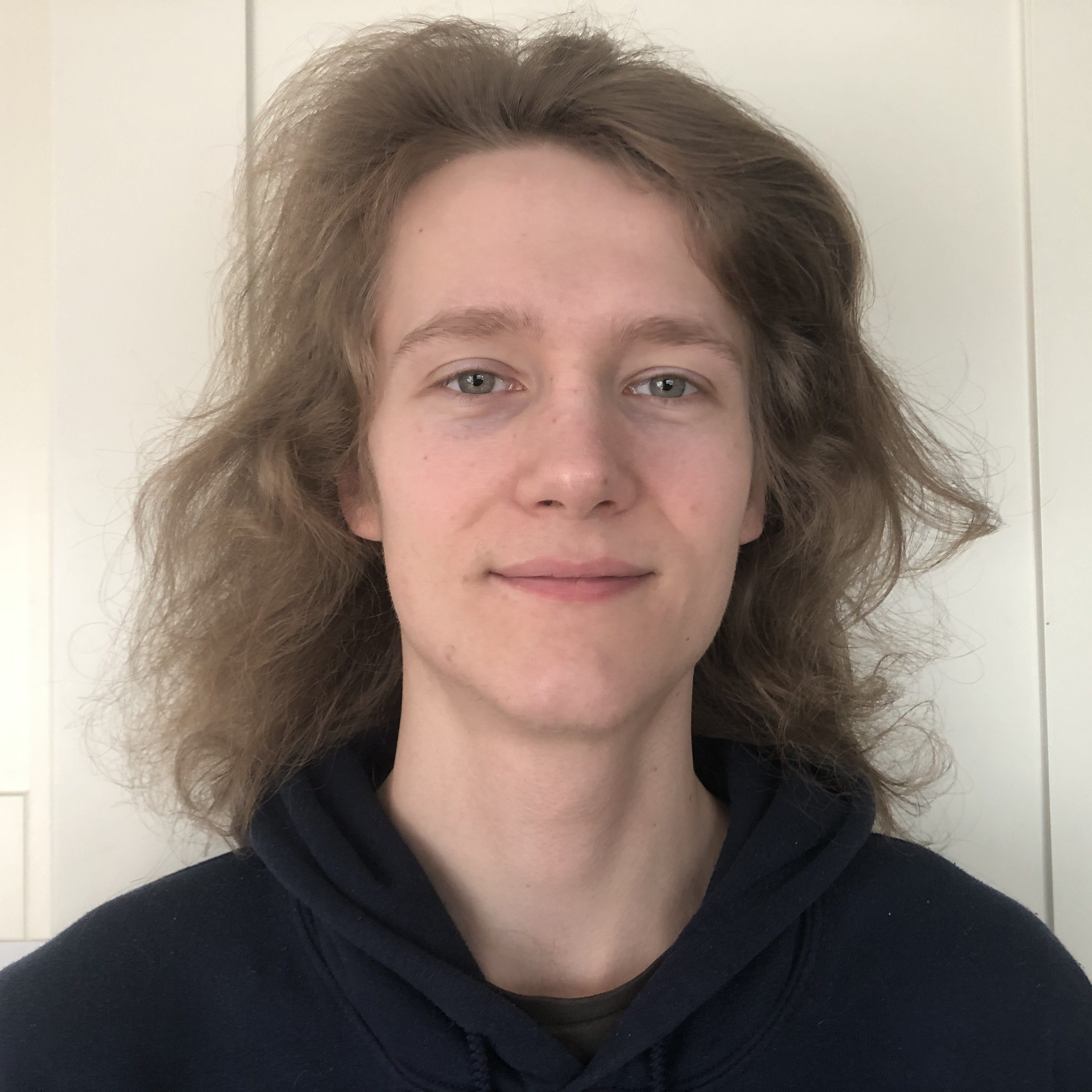 Headshot of Oli, a white man in his early 20's with long curling brown hair.