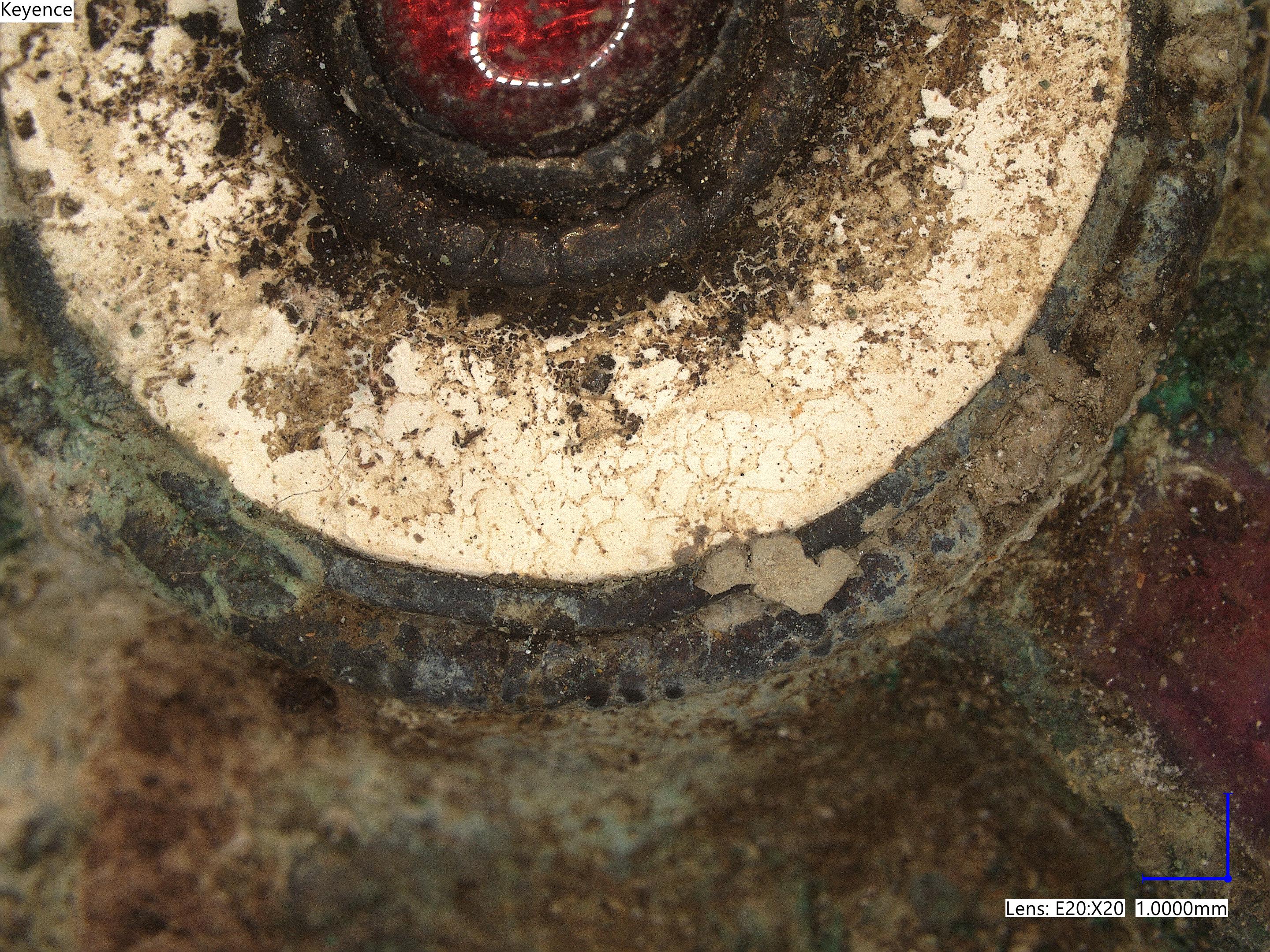 Microscope close-up of a brooch, showing tiny details of flaking metals and the cut marks in the red gemstone