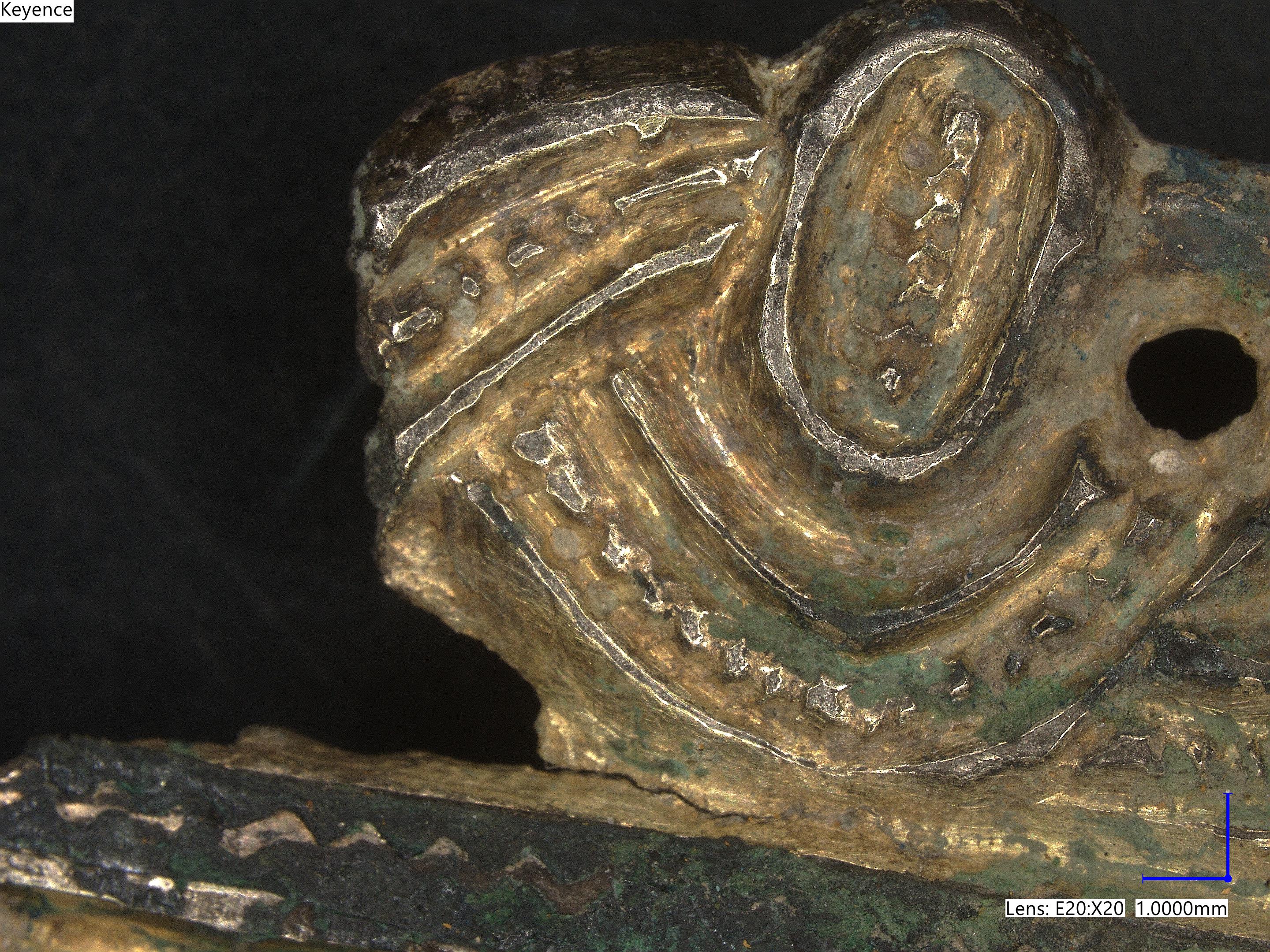 Microscope photograph of a gold brooch showing lots of detailed ridges and bumps, worn down with age
