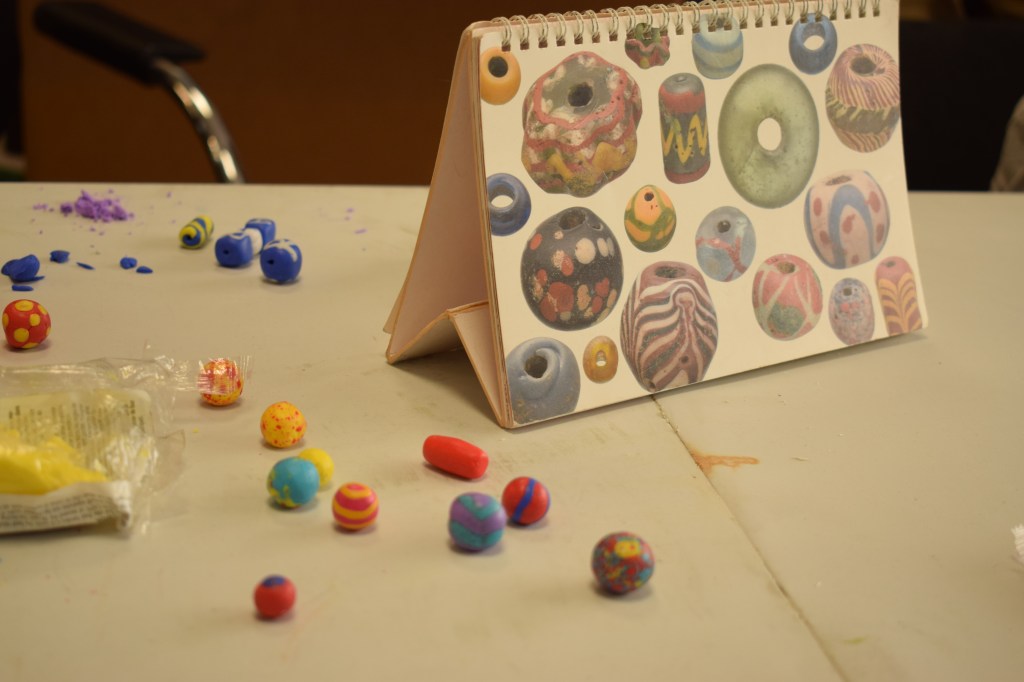 Multicoloured clay beads next to a poster of original Anglo-Saxon beads of the same style