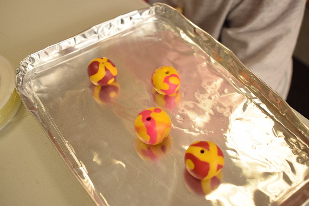 Multicoloured clay beads on a silver tray ready for baking