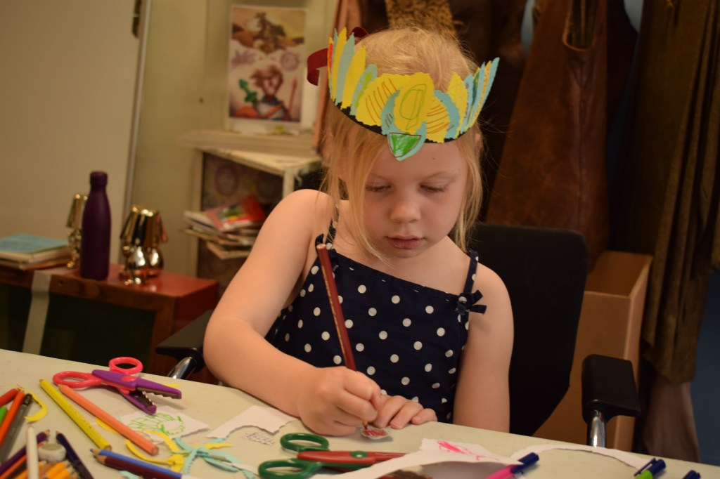 A girl draws a Roman coin design while wearing a card laurel wreath on her head