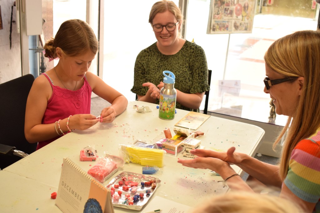 Emma, an adult and a child all making clay beads at the workshop, rolling out clay in their hands