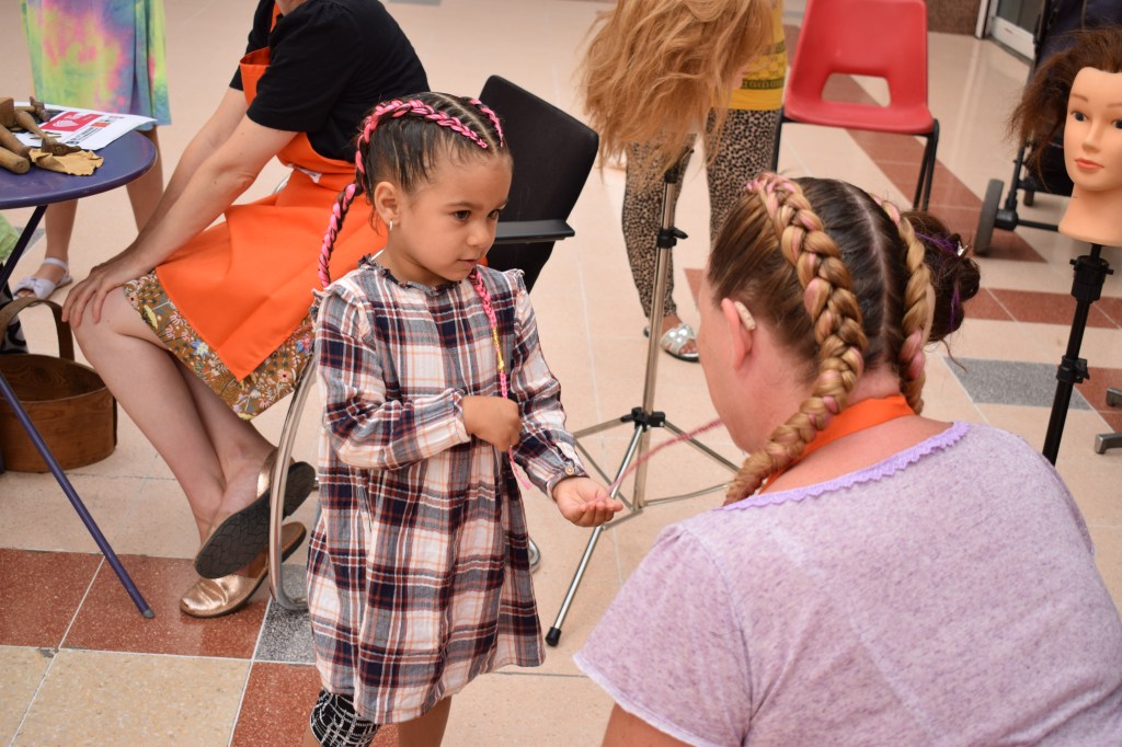 Liz with braided hair talks to a small girl with matching bright pink braids