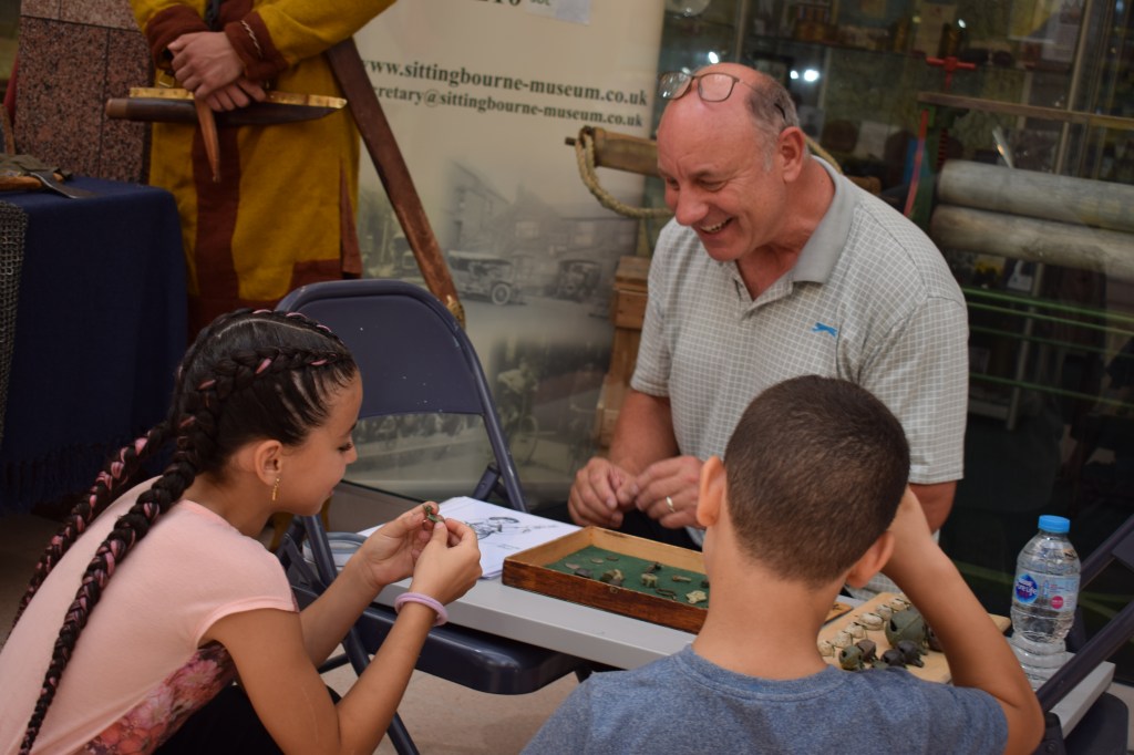 A girl and boy inspect an object from Andy's tray of finds