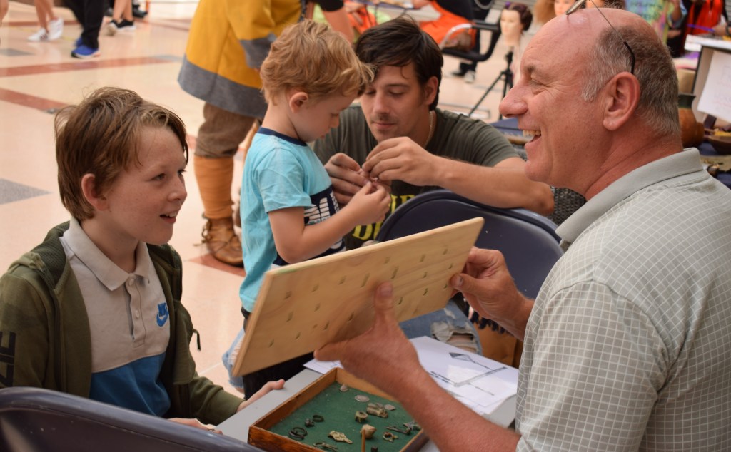 Andy demonstrates how the bells sound by shaking them on a wooden board, watched by a group of boys