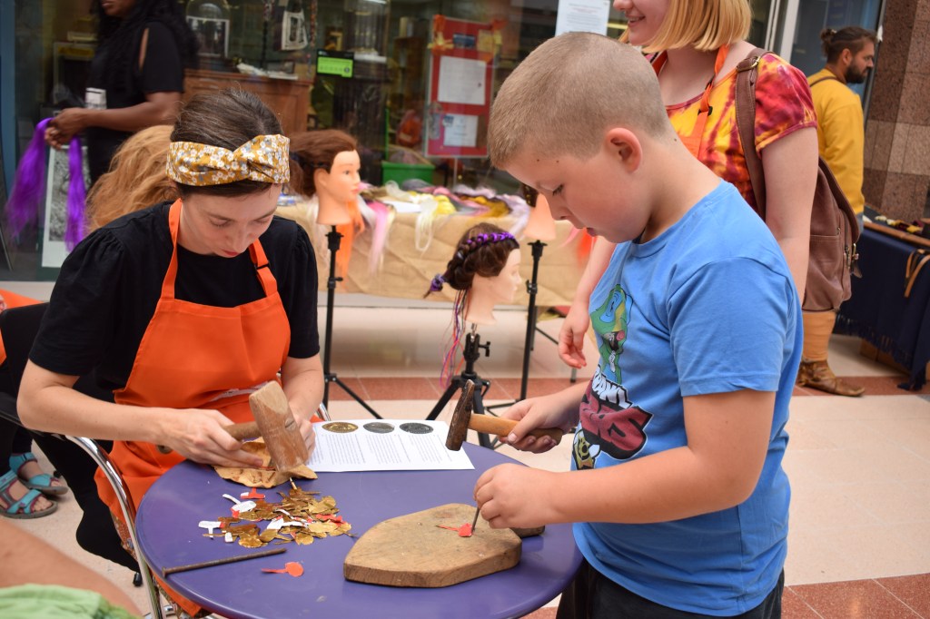 Young boy doing some metalworking with a hammer helped by Emma