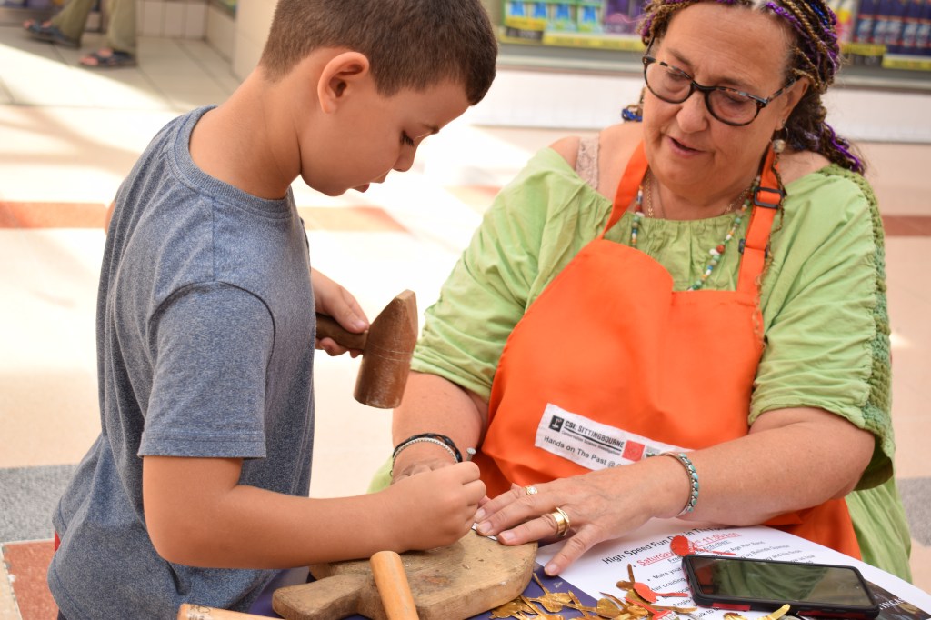 Young boy doing some metalworking with a hammer helped by Dana